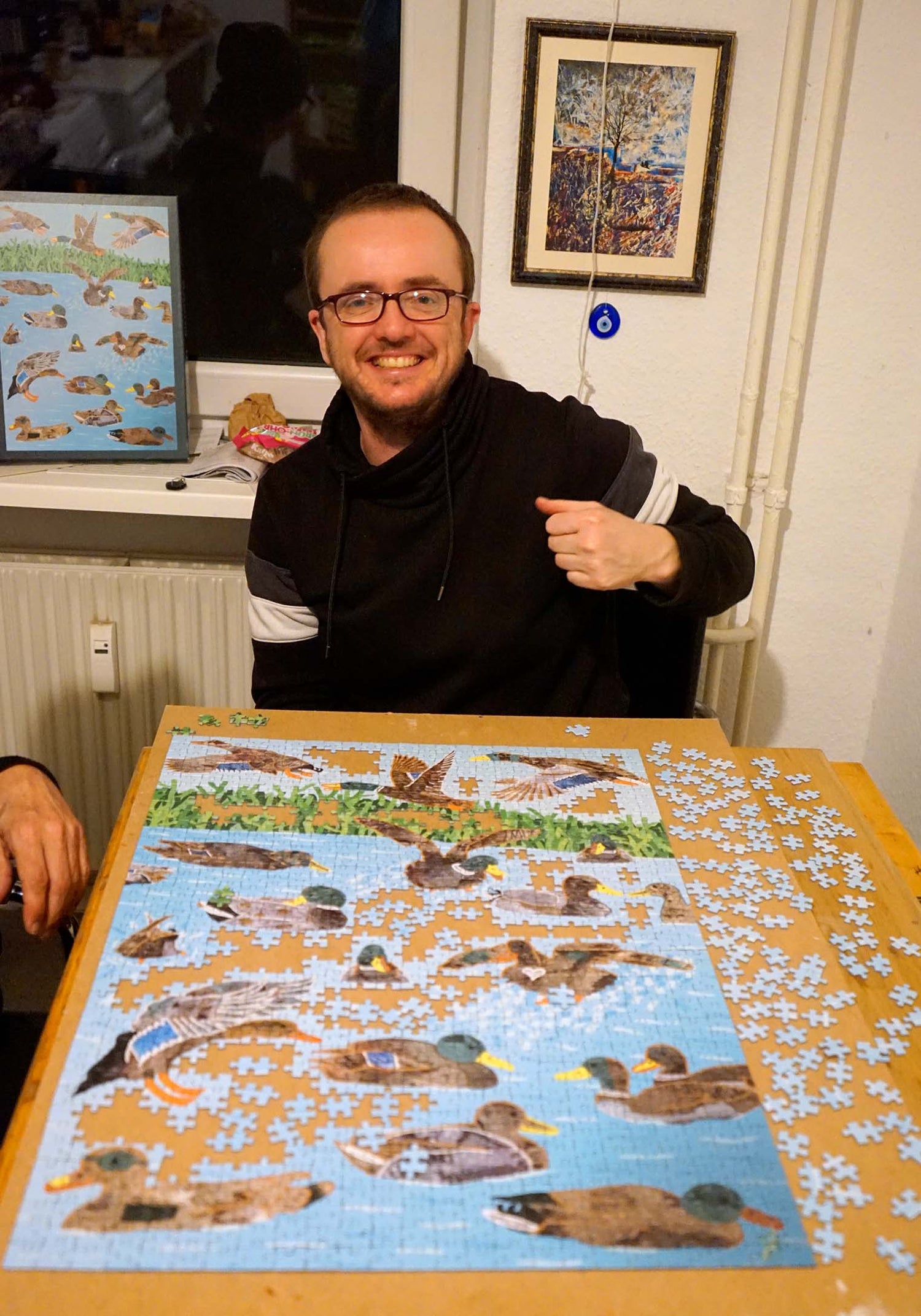 The artist Katja Anton Cronauer sits at a kitchen table with a puzzle of his artwork, TIN Ducks.