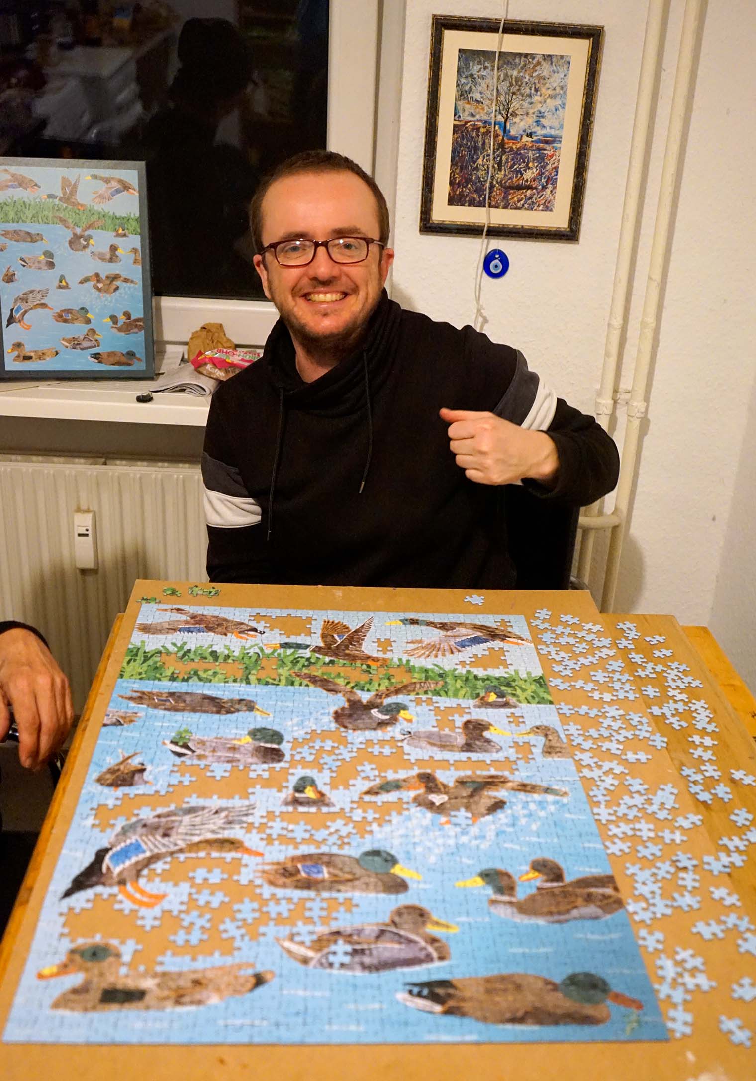 The artist Katja Anton Cronauer sits at a kitchen table with a puzzle of his artwork, TIN Ducks.