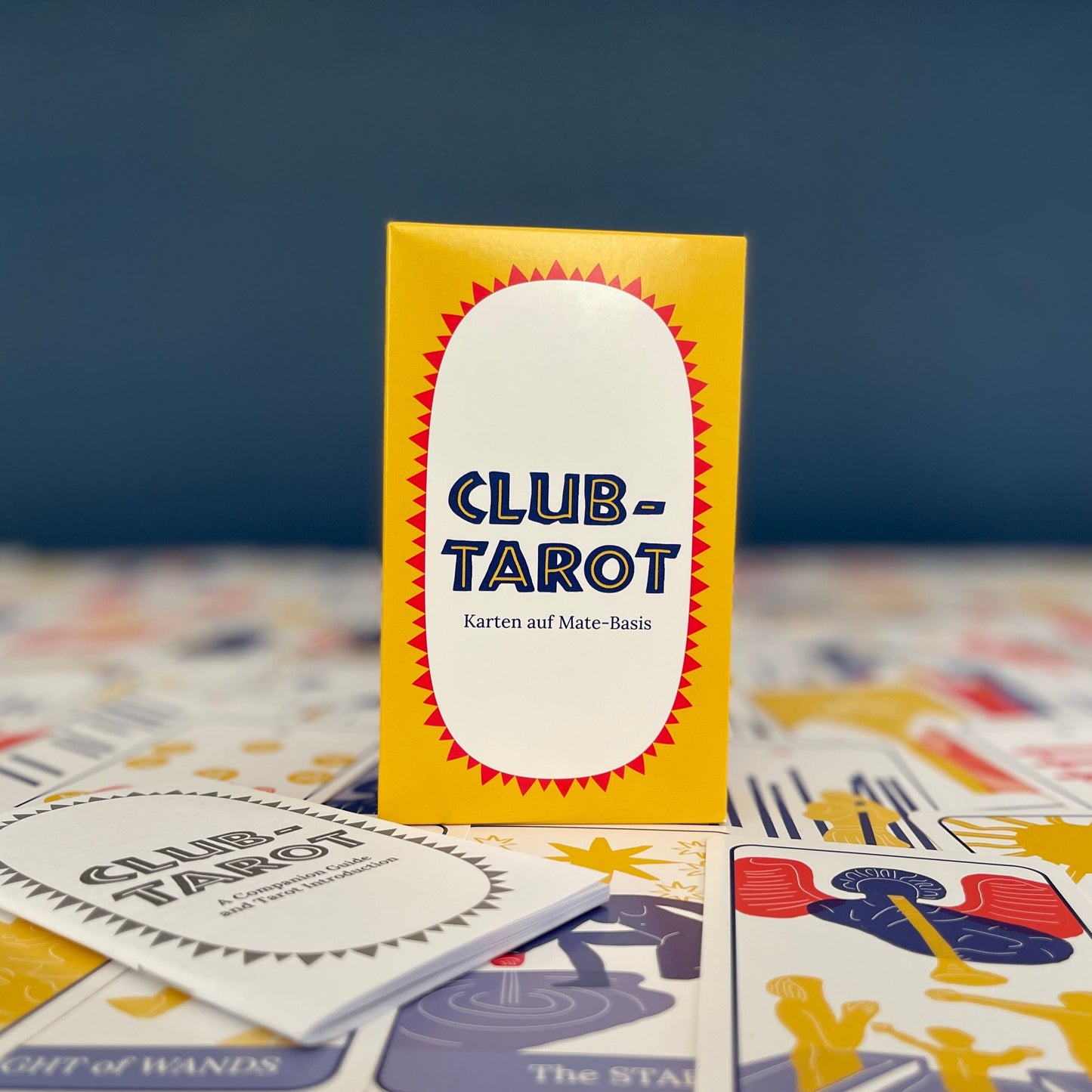 A colorful boxed deck of Tarot cards sits on the cards laid out, with the guidebook nearby. Against a dark blue background.
