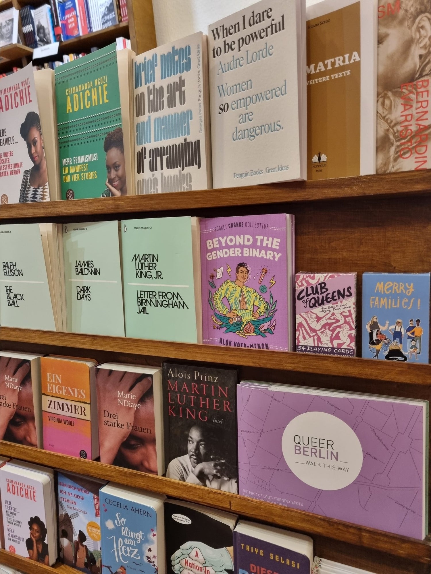 Decks of playing cards on a bookshelf next to Alok Vaid-Menon's "Beyond The Gender Binary" and a map of Queer Berlin.