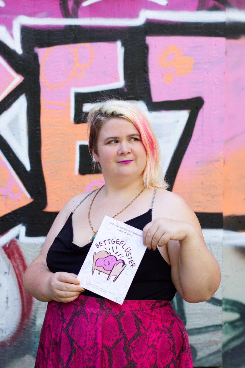 Porträt von Mercedes von Kulessa, vor einem unscharfen Hintergrund im Freien. Sie hat helle Haut und rosa Haare und lächelt.