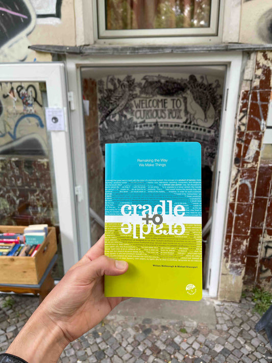 Hand holding blue and green "Cradle to Cradle" book in front of a bookstore in Berlin.