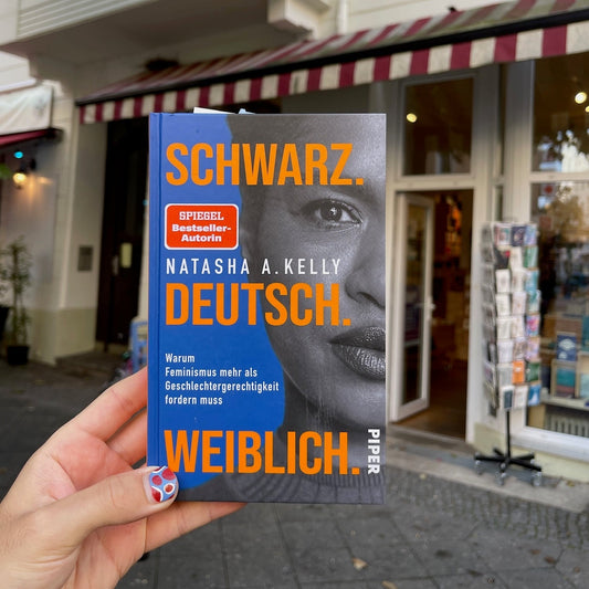 Hand holding Scwharz. Deutsch. Weiblich. book by Natasha Kelly in front of Odradek Bookstore in Berlin Schöneberg