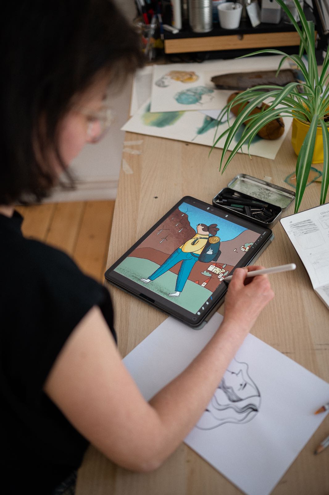 A photograph over the shoulder of artist Clara Gilod in her art studio in Berlin Germany. On her iPad is a character wearing a backpack, from the game Merry Families. 