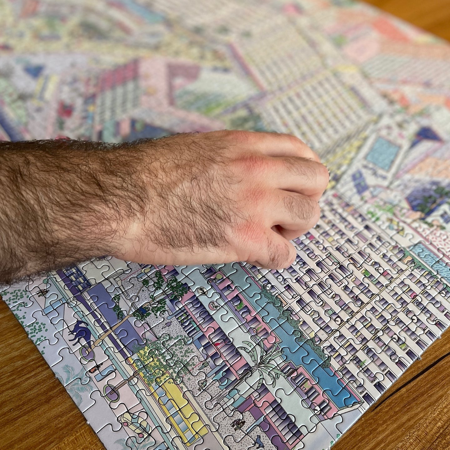 A light-skinned, dark-haired hand places a last piece onto a puzzle with an illustration of Kottbusser Tor with dinosaurs.