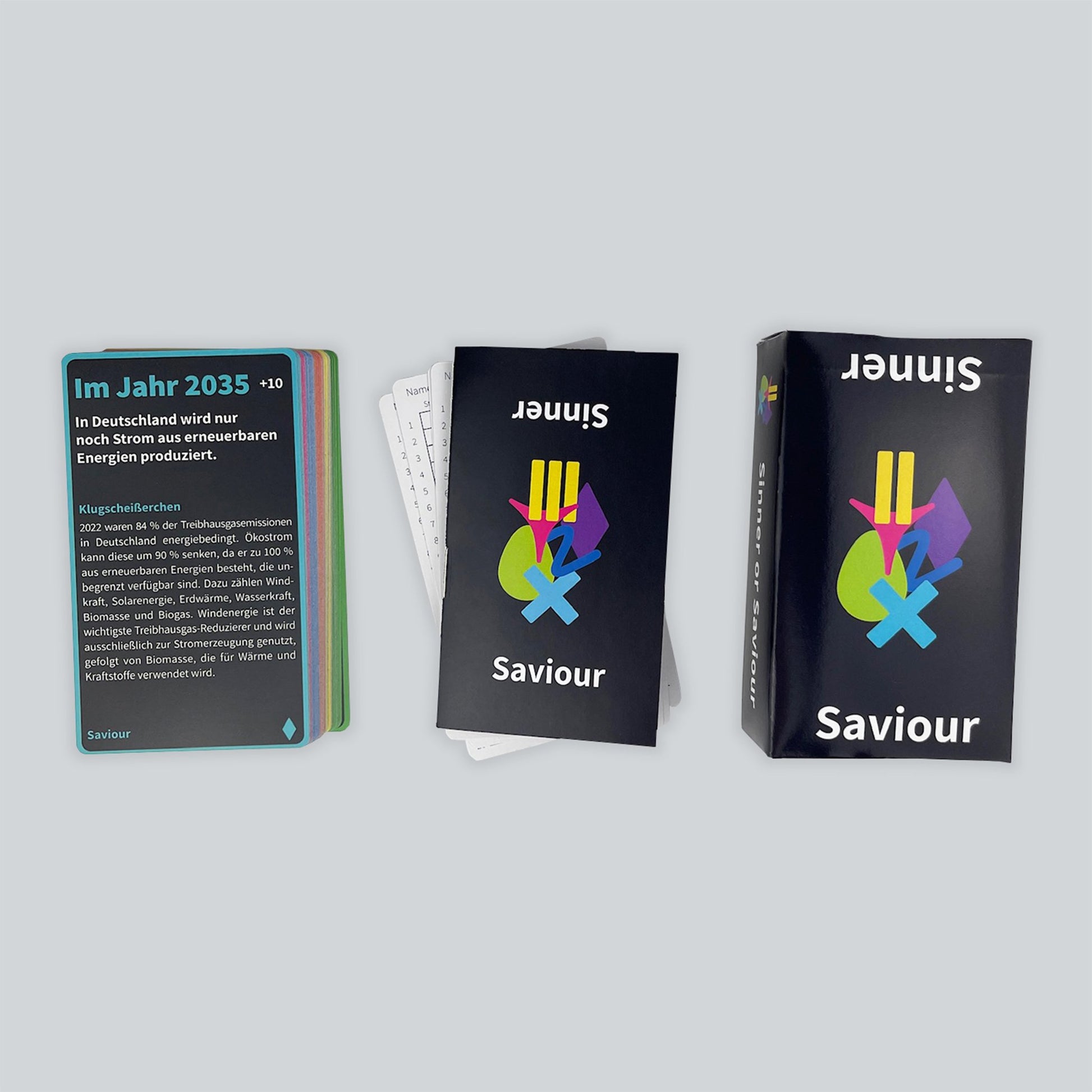 A boxed set of the card game Sinner or Saviour against a gray background. On the left is a stack of cards, in the middle is a guidebook on top of scorecards, and the box is on the right.