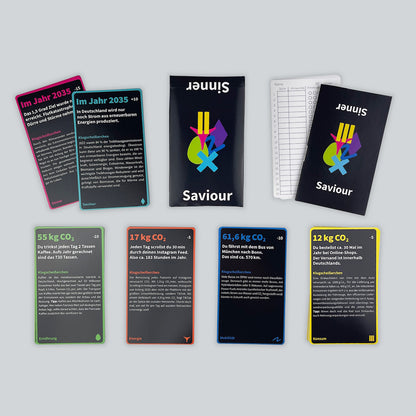 A view of the educational game Sinner or Saviour from above. Cards are stacked in 6 categories (Mobility, Energy, etc.), with the box, scorecards, and guidebook against a light gray background.