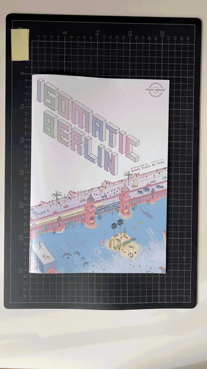 GIF showing how to cut apart Polar Embassy's Isomatic Berlin coloring book, and create one of the wall posters. Jon Derman Harris' hands cut the book with a mat knife, then tape 9 A4 pages together to create a wall poster, that he hangs on a wall at the end.