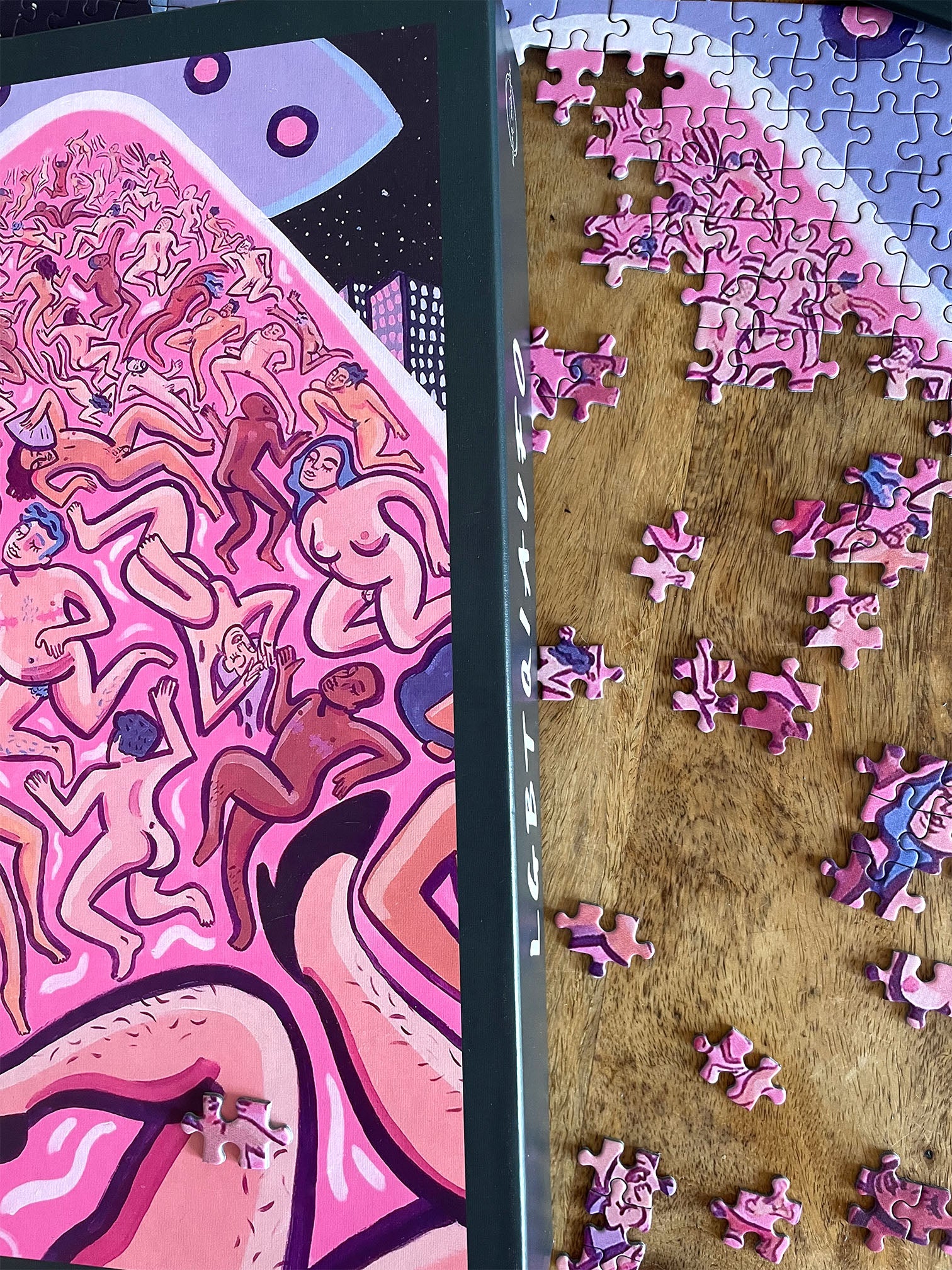 Polar Embassy's puzzle by Rory Midahni, with queer and trans people being beamed up by UFOs. The puzzle box lays on a wooden table on top of the partially-completed puzzle.
