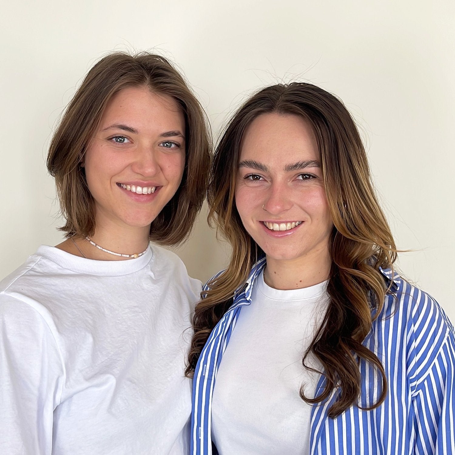 A professional photo of Luisa Schrott and Maike Klingler, designers of Sinner or Saviour, against a creme background. They are both smiling, looking at the camera. 
