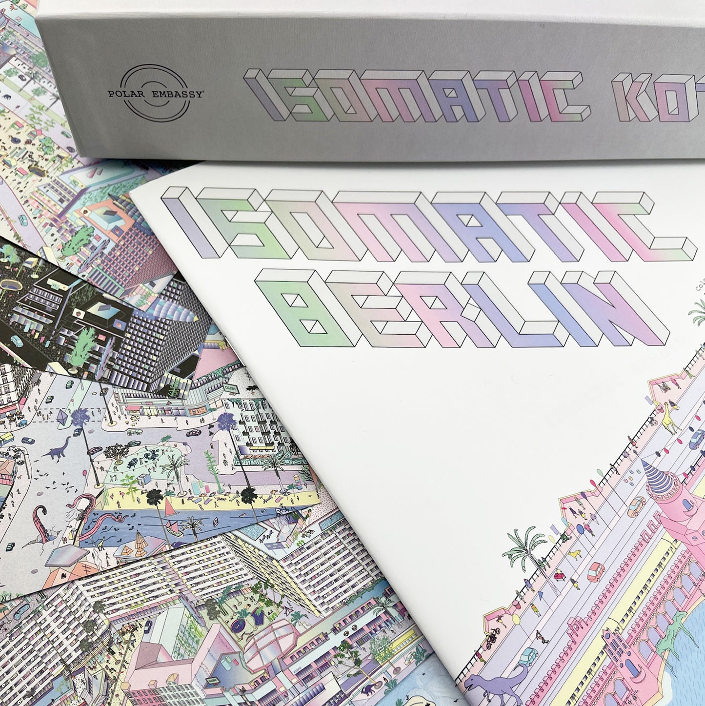 A photo of a puzzle with a "Polar Embassy" logo, and the title "Isomatic Kotti" sits on top of a coloring book titled "Isomatic Berlin". Below the coloring book are postcards with colorful designs of Berlin Kreuzberg with dinosaurs and wild animals.