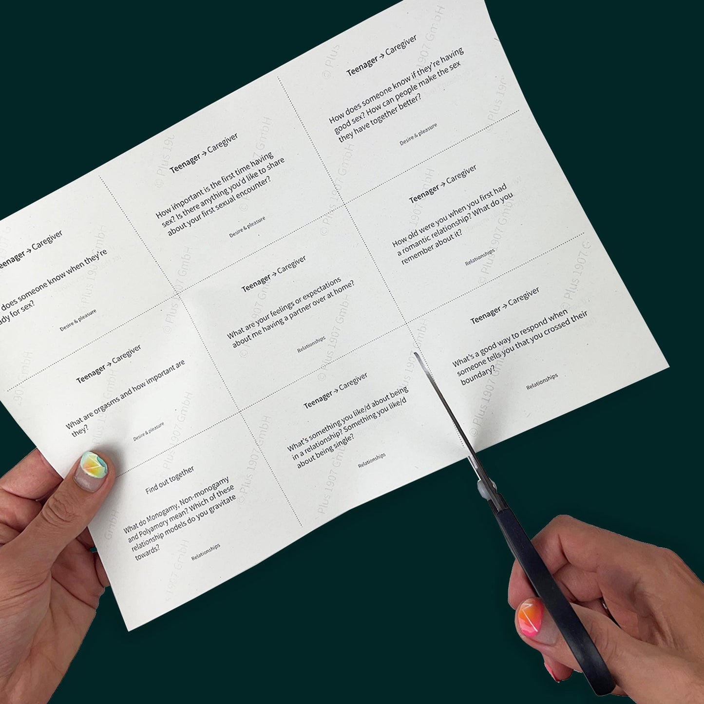 A hand with bright nail polish cuts along a dotted line on a piece of paper. The hand is cutting out cards with sex education questions for teens and families. Some questions include "What's a good way to respond when someone tells you that you crossed their boundary?" and "What do Monogamy, Non-monogamy, and Polyamory mean? Which of these relationship models do you gravitate towards?"