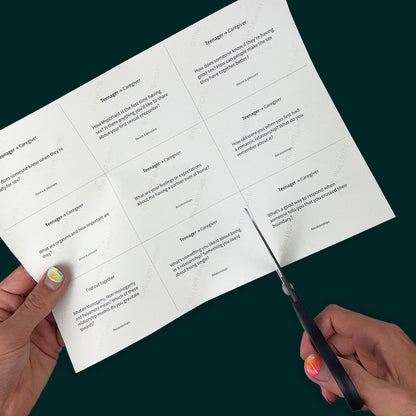 A hand with bright nail polish cuts along a dotted line on a piece of paper. The hand is cutting out cards with sex education questions for teens and families. Some questions include "What's a good way to respond when someone tells you that you crossed their boundary?" and "What do Monogamy, Non-monogamy, and Polyamory mean? Which of these relationship models do you gravitate towards?"