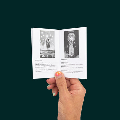 A hand with bright pink nail polish holds the guidebook from The Ancestral Healing Tarot Deck by Care for Polar Embassy. The black and white pages show The Star and The Moon cards.