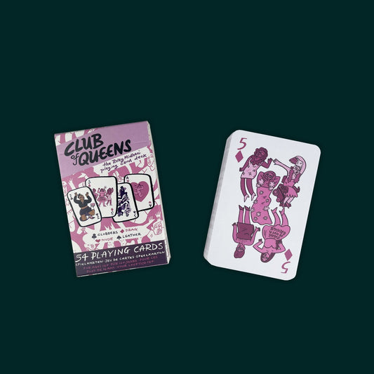 A pink and purple box of playing cards next to a stack of cards with the three of diamonds on top. On the card are three drag queens, the middle wearing a dress that says "Drag is not a crime".