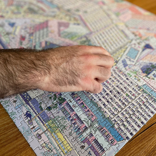 Hand places final piece in Berlin jigsaw puzzle of Kottbusser Tor cityscape with playful dinosaurs.