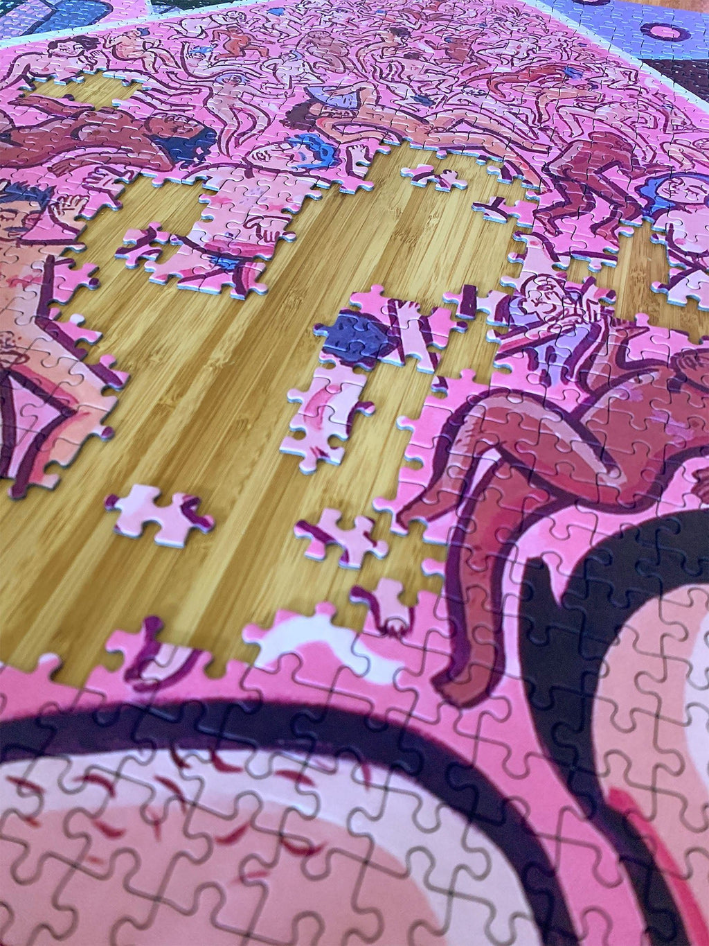 Close-up of queer jigsaw puzzle showing LGBTQIA people in pink UFO beam, incomplete on light wooden table.