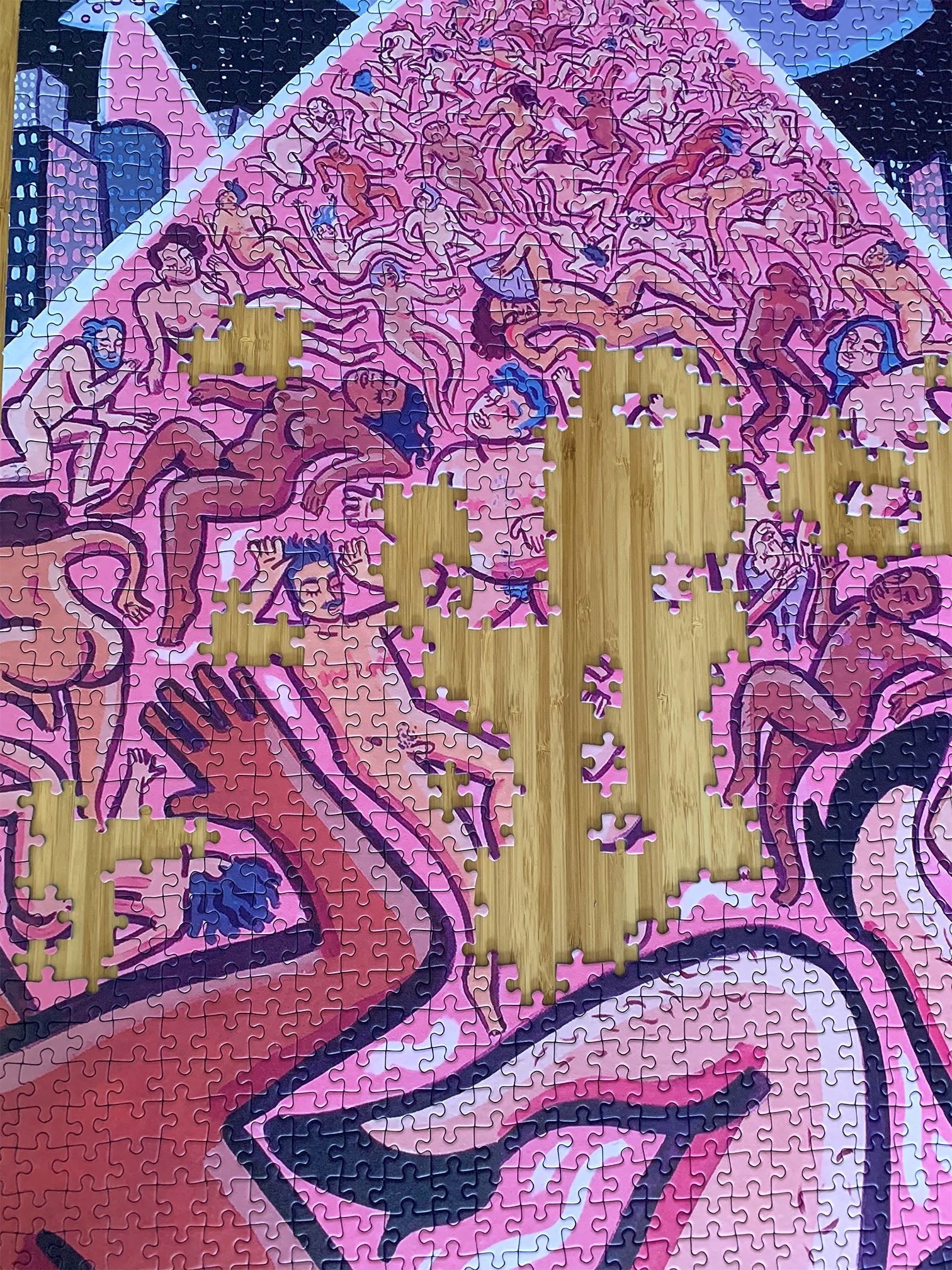 Nearly finished queer jigsaw puzzle 1000 pieces with pink UFO beam lifting trans figures, on wooden table.