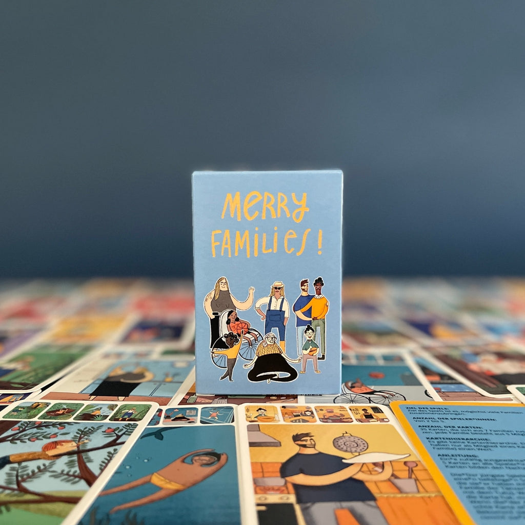 Merry Families inclusive kids card game box standing on cards, against blue background.