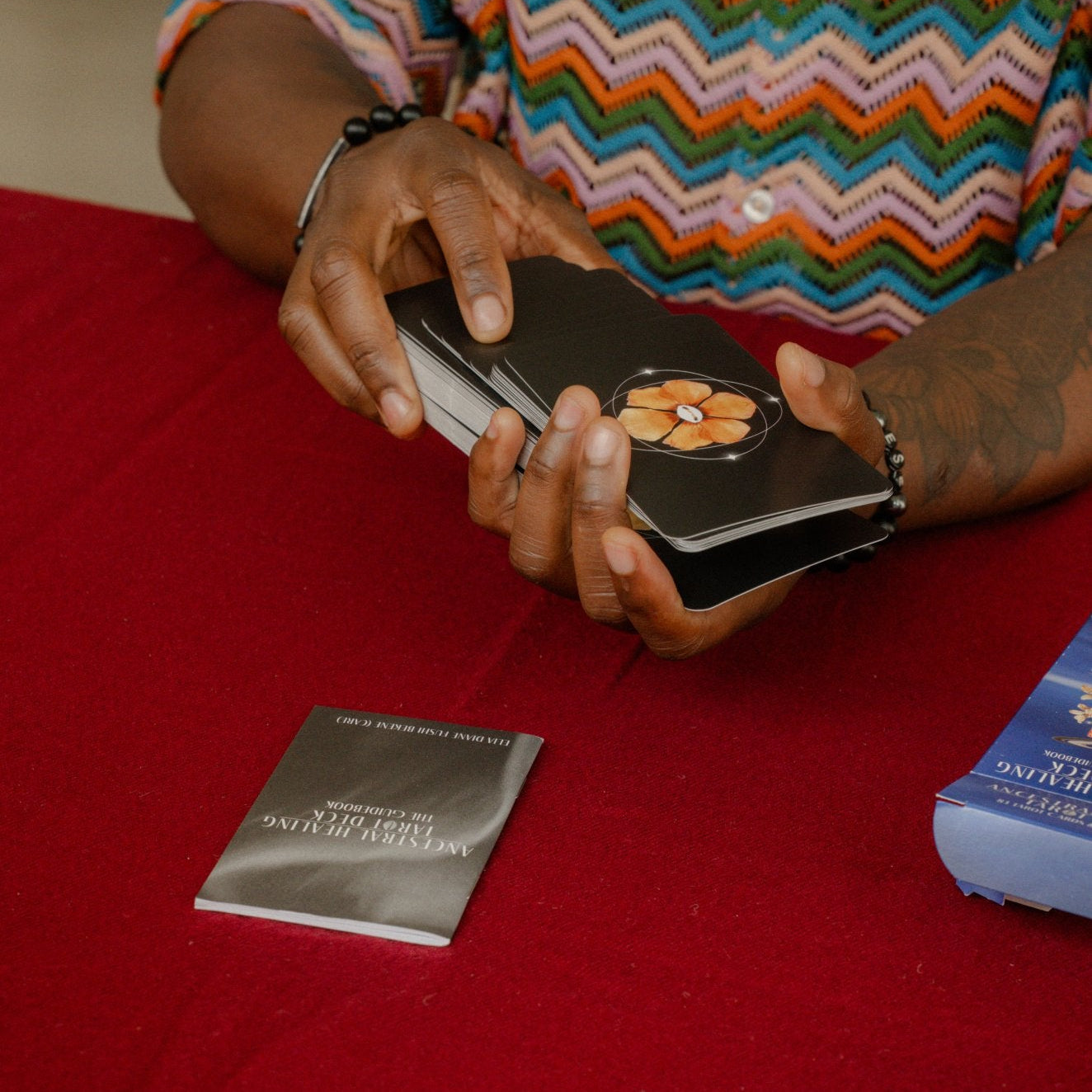 Hands shuffling the Ancestral Healing Tarot deck by the artist Care over a red cloth.