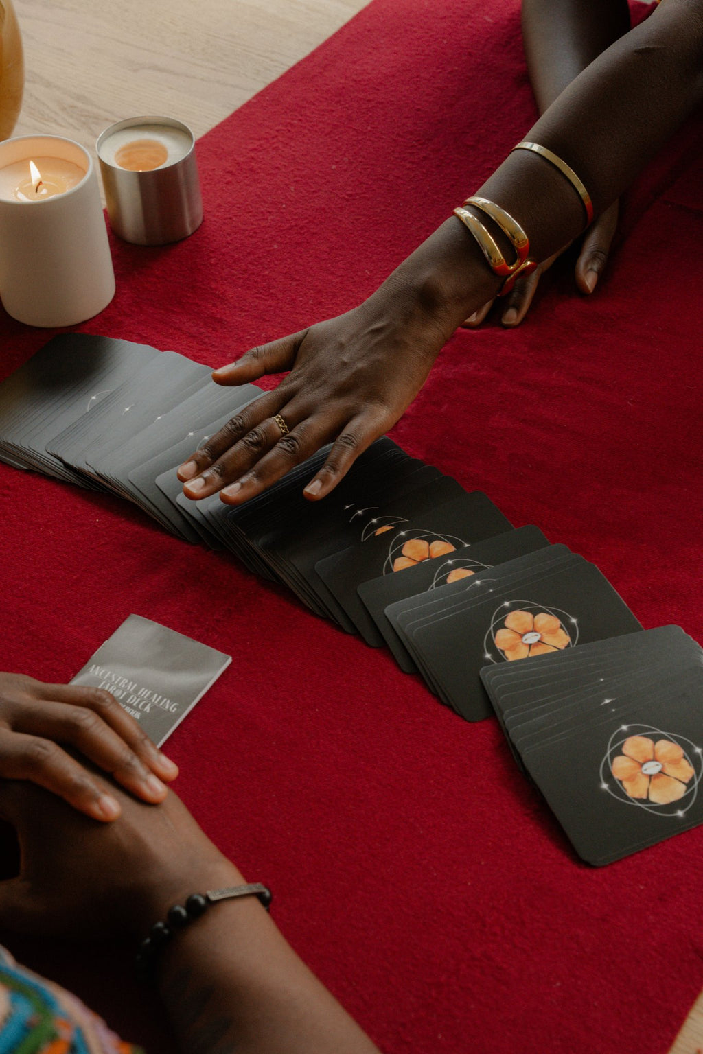 Hands laying out an Ancestral Healing Tarot spread by artist Care on a black reading mat.