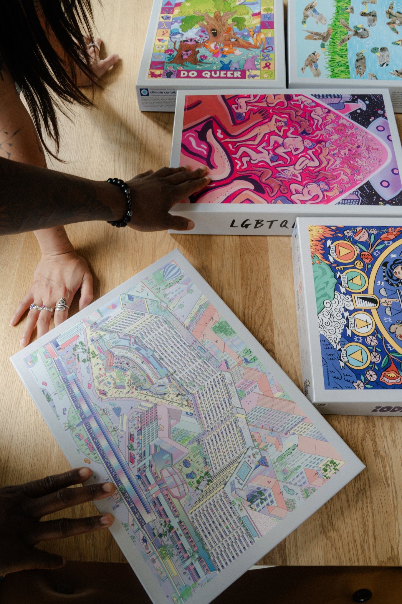 Hands choosing between Polar Embassy's jigsaw puzzles spread across a wooden table.