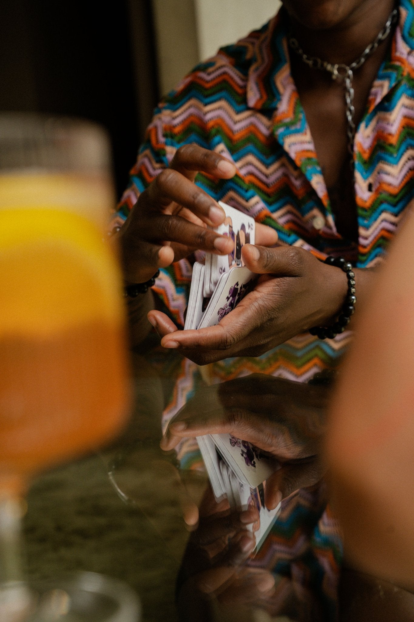 Hands shuffling Rory Midhani's Club of Queens queer playing cards over a glass table.