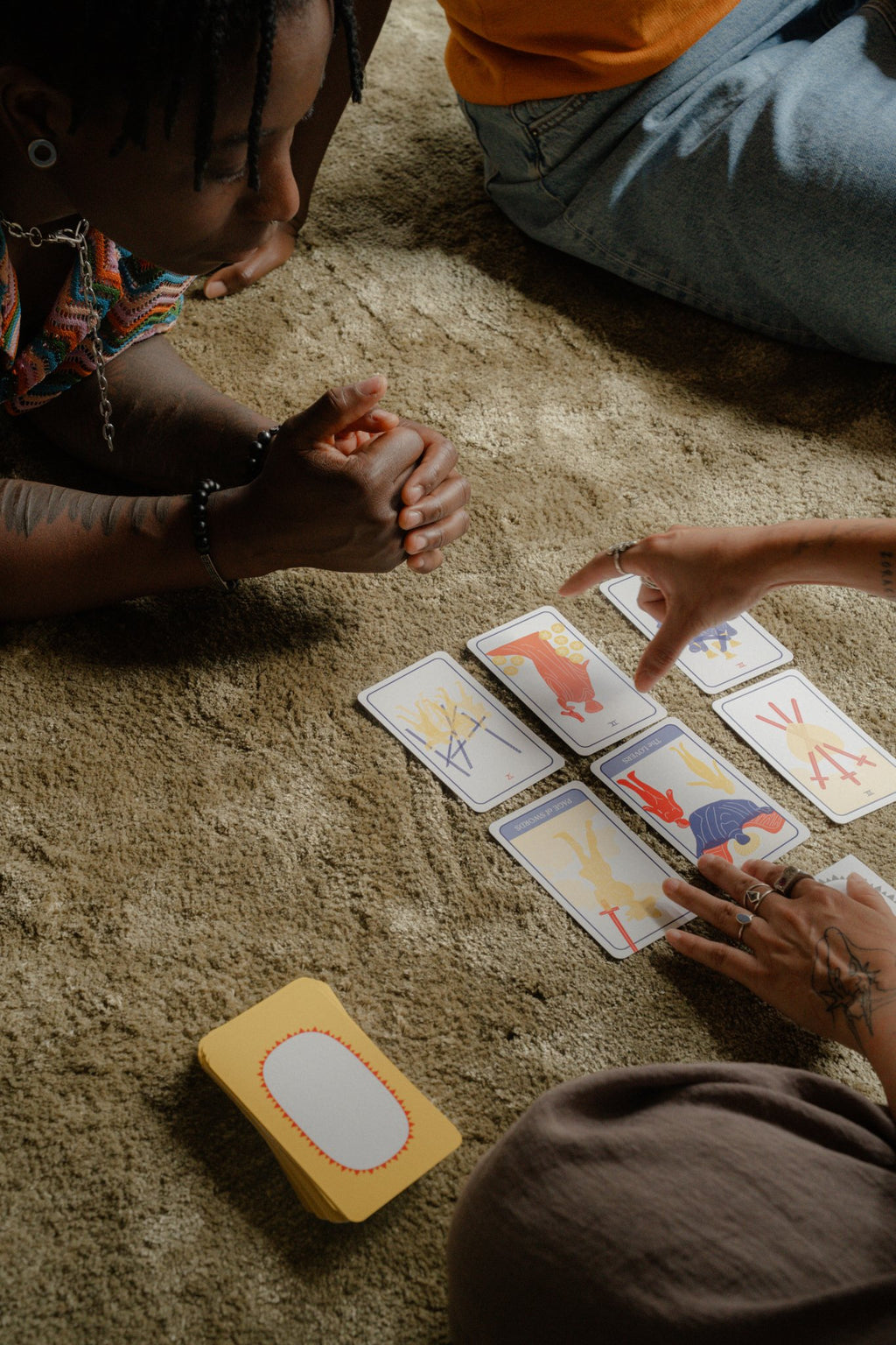 Hands pointing to a 6-card spread of Club Tarot on a carpet, with the querent and a friend look on.