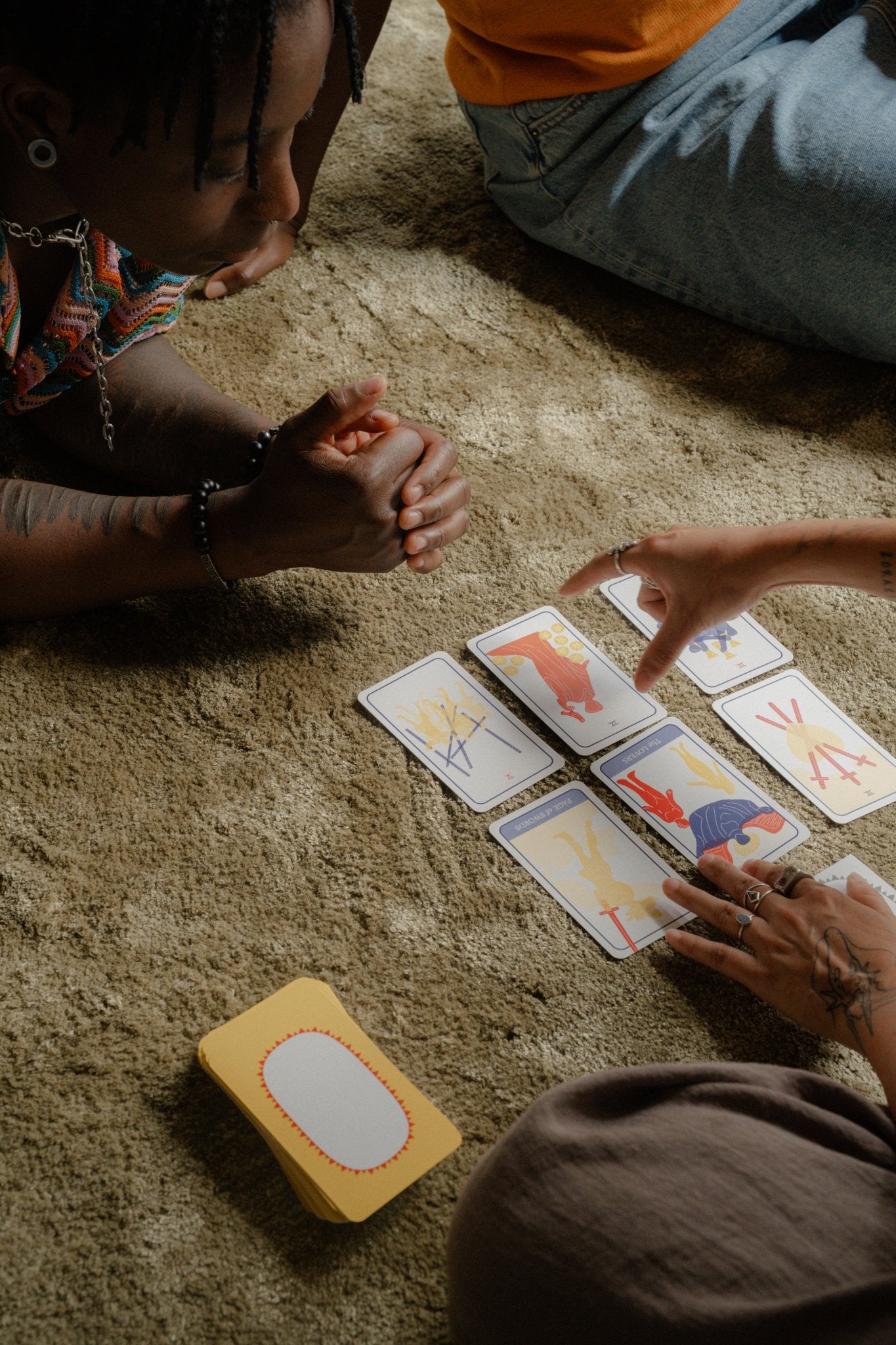 Hands pointing to a 6-card spread of Club Tarot on a carpet, with the querent and a friend look on.