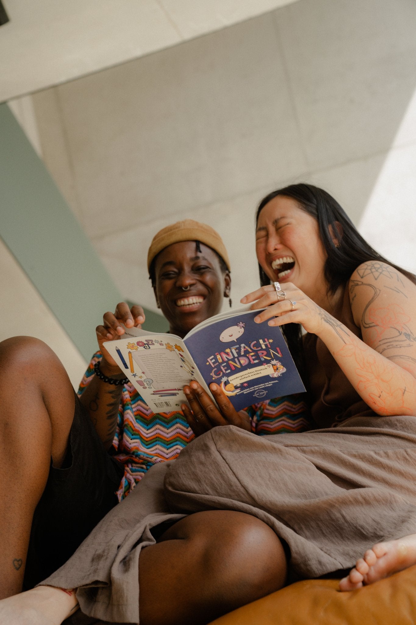 Zwei Personen lachen beim Lesen von Einfach Gendern, dem Arbeitsbuch für gendergerechtes Deutsch.