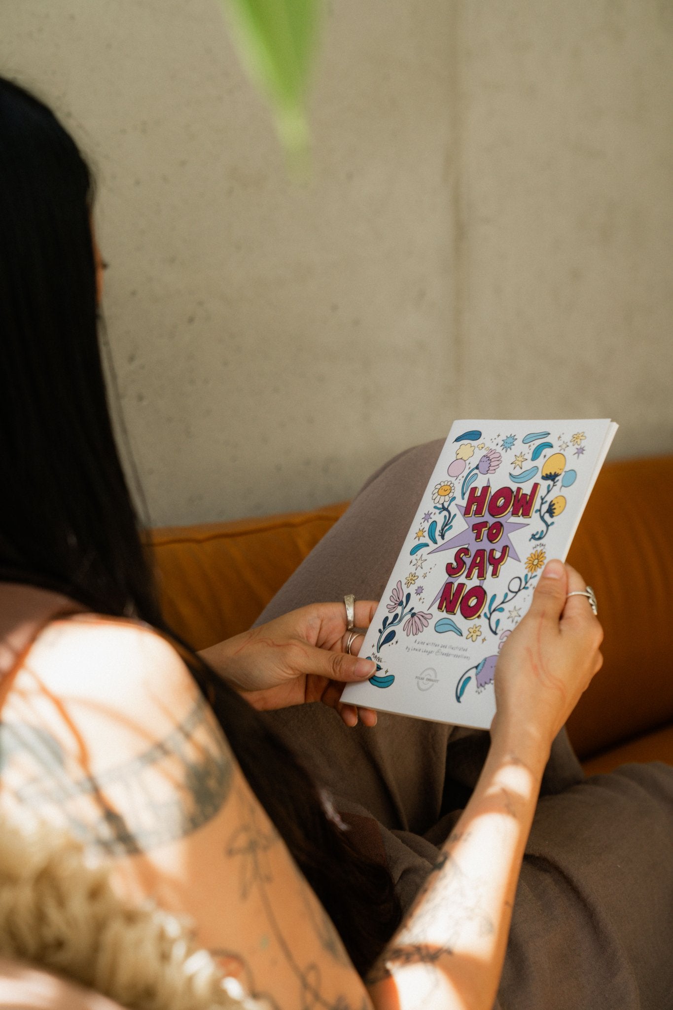 Hands holding the How to Say No workbook on consent and boundaries, illustrated by Louie Läuger.