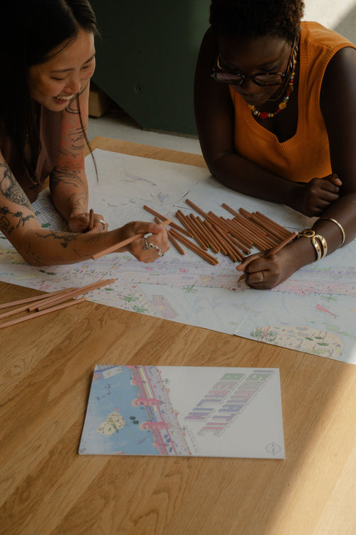 Two people colour the Berlin Coloring Book for adults at a wooden table, Isomatic art by Bruno Pinto da Cruz.
