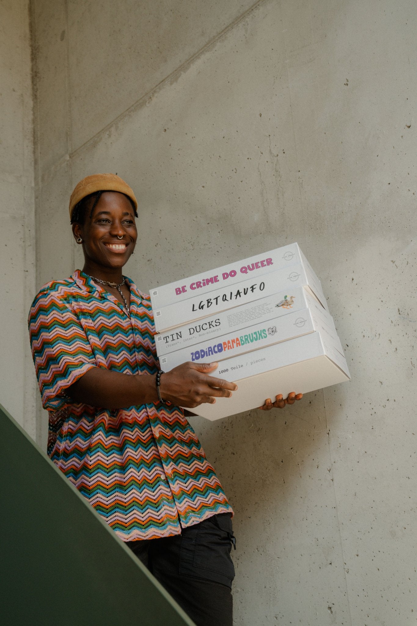 Person holding a stack of Polar Embassy's jigsaw puzzles: Be Crime, LGBTQIAUFO, TIN Ducks and Zodíaco.