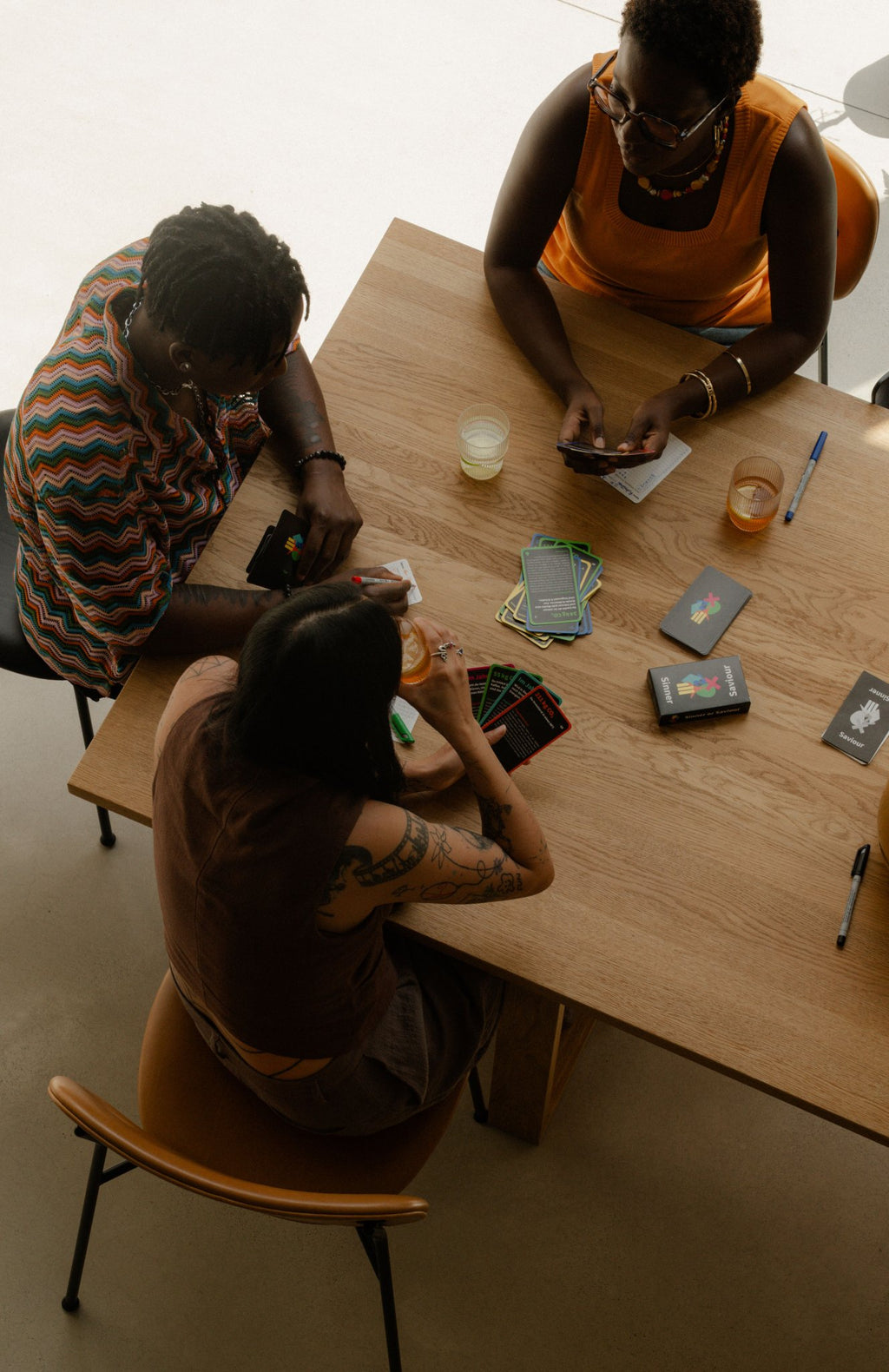 Drei Personen spielen Sinner or Saviour, das Klimabildungs-Kartenspiel von Polar Embassy, am Tisch.