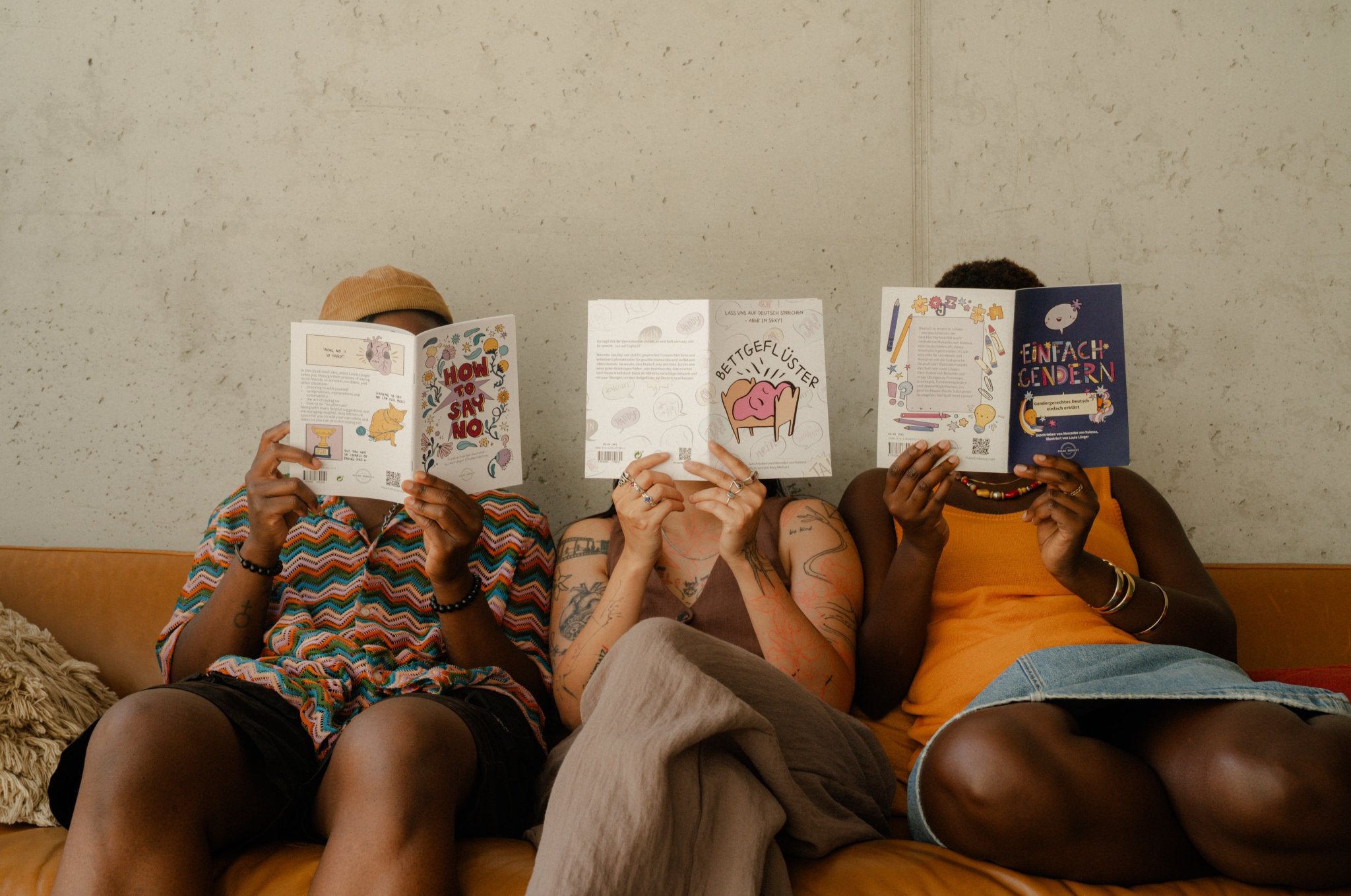 Three friends hold up Polar Embassy workbooks on a couch: consent, gender-inclusive language and dirty talk.